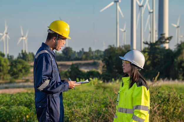 Фото Два инженера, работающие и держащие отчет на ветряной электростанции, электростанции на горе, люди в таиланде. техник, мужчина и женщина, обсуждают работу