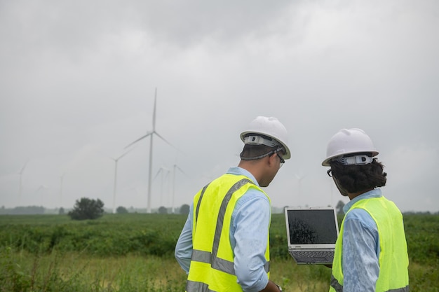 Two engineers working and holding the report at wind turbine farm Power Generator Station on mountainThailand people