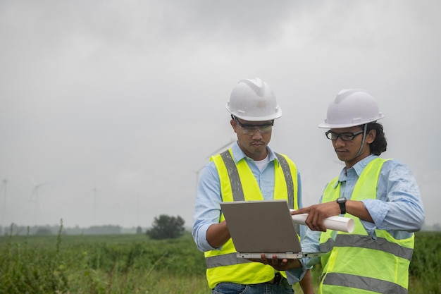 Two engineers working and holding the report at wind turbine farm Power Generator Station on mountainThailand people