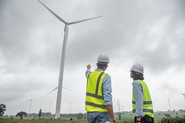 Two engineers working and holding the report at wind turbine farm Power Generator Station on mountainThailand people