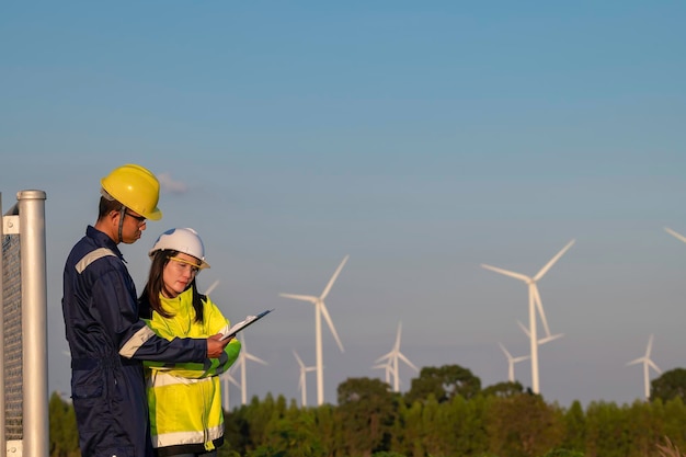 Photo two engineers working and holding the report at wind turbine farm power generator station on mountainthailand peopletechnician man and woman discuss about work