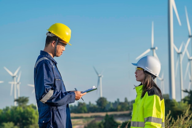 Two engineers working and holding the report at wind turbine farm Power Generator Station on mountainThailand peopleTechnician man and woman discuss about work