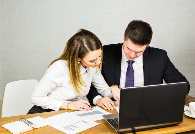 Two entrepreneurs sitting together working in an office desk comparing documents.
