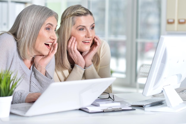 Two excited mature women using laptop and computer