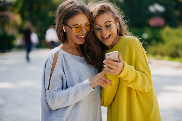 Due belle donne eccitate si divertono insieme ascoltano musica, guardano gli smartphone e sorridono