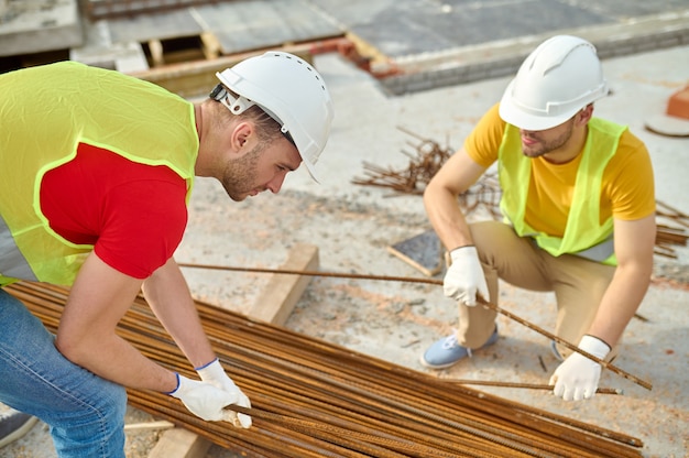 Two experienced workers in safety vests and hardhats choosing rebars