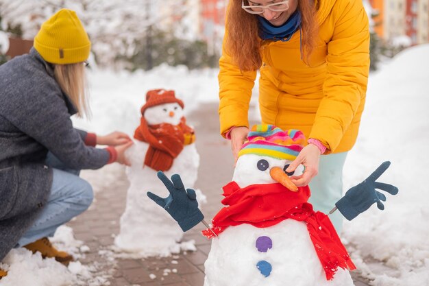 写真 2人の顔のない白人女性が雪だるまを作っています 冬の女の子が楽しんでいます