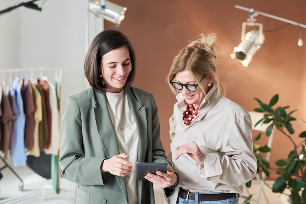 Two fashion designer watching something on tablet pc and smiling during their work in workshop