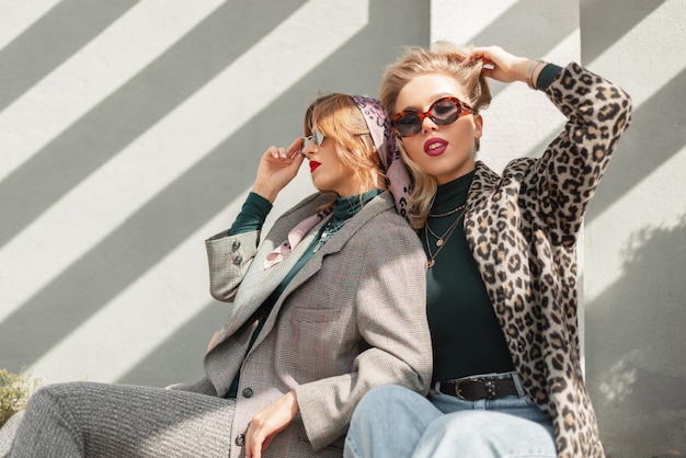 Two fashion glamorous girls friends in trendy outfit sits and poses in the city