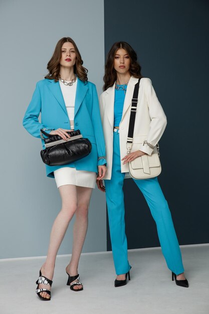 Two fashion models in aqua blue white looks Jacket blazer skirt top pants trousers handbags