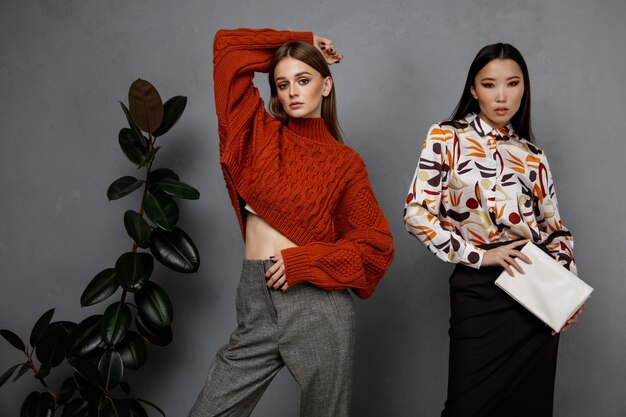 Photo two fashion models in sweater shirt black skirt gray pants trousers textured wall tall flower