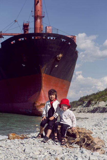 ノヴォロシースク沖で座礁した大きなリオ船の隣に2人のファッショナブルな男の子が座っています