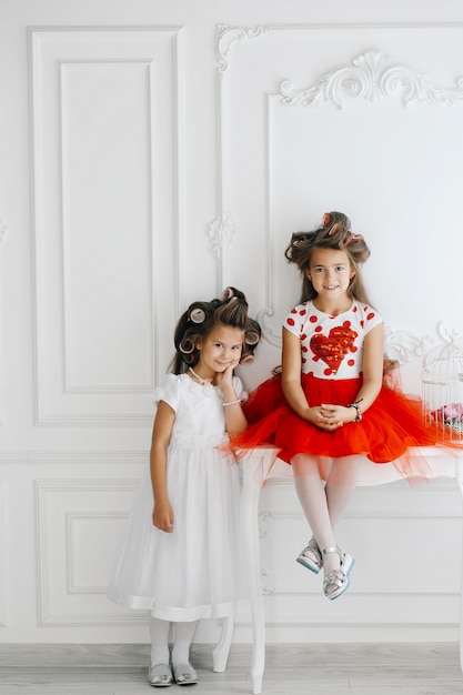 Two fashionable mother's little princesses in hair curlers looking at each other and smiling