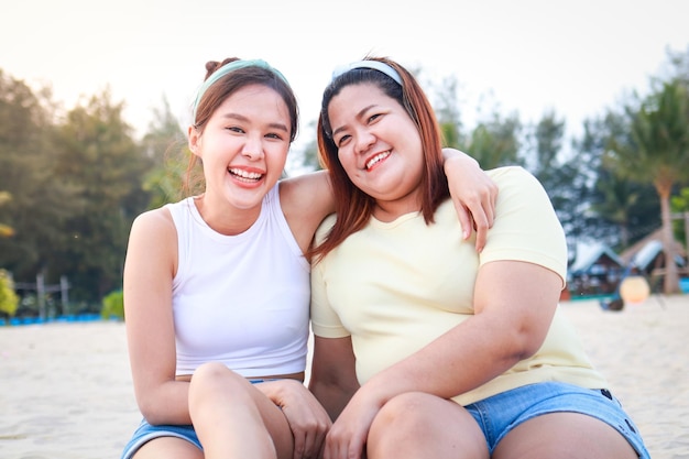 Foto due ragazze asiatiche grasse e magre che si divertono godendosi il turismo marittimo seduti sulla spiaggia