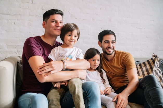 Two fathers and their kids enjoying time together while watching movies on the sofa at home. Family concept.