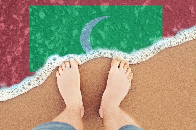 Two Feet on sandy beach with flag Maldives Top View on sea surf