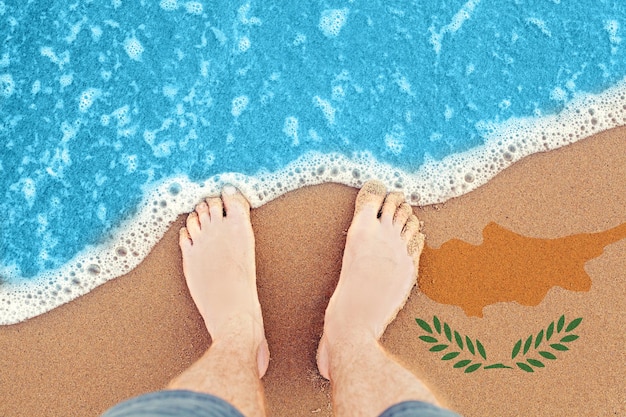 Two Feet on the sunny sandy beach with flag Cyprus Top View on surf