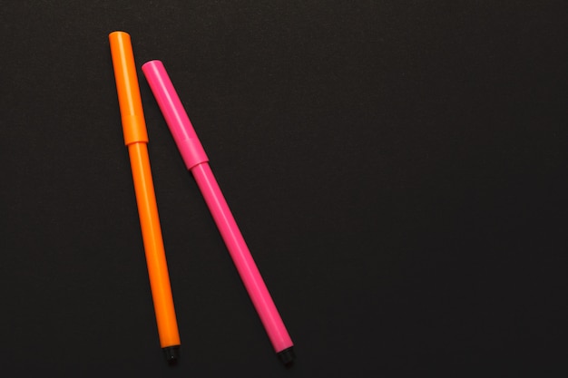 Two felt-tip pens of pink and orange colors on black paper 