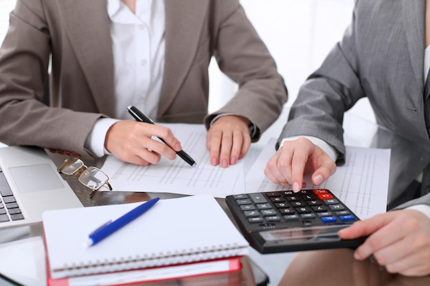Two female accountants counting on calculator income for tax form completion hands closeup. Internal Revenue Service inspector checking financial document. Planning budget, audit  concept