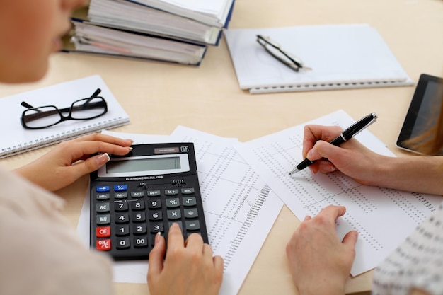 Two female accountants counting on calculator income for tax form completion hands closeup. Internal Revenue Service inspector checking financial document. Planning budget, audit  concept