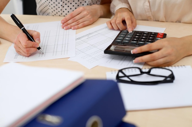 Two female accountants counting on calculator income for tax form completion hands closeup. Internal Revenue Service inspector checking financial document. Planning budget, audit  concept