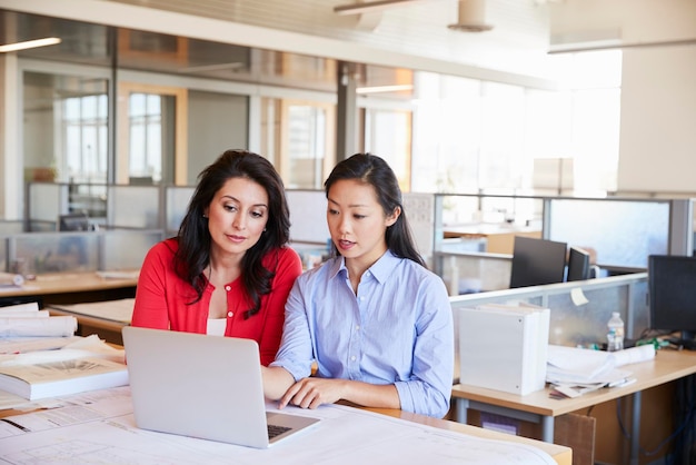 Two female architects using a laptop in an open plan office