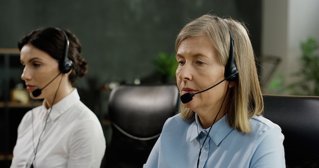 두 여성 콜 센터 근로자 테이블에 앉아 컴퓨터의 키보드 입력 및 헤드셋 클라이언트와 얘기.