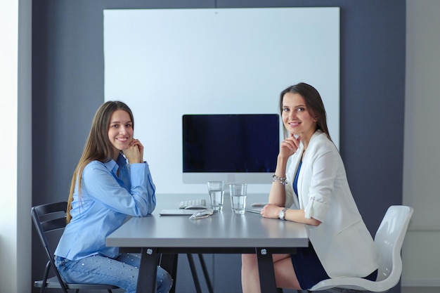 Две коллеги-женщины в офисе сидят на столе