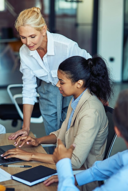 Two female colleagues using laptop and discussing something while working together in the modern