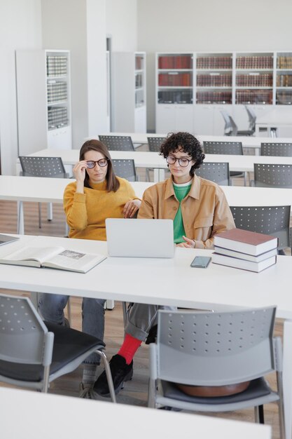 Two female colleagues work on laptops in coworking office library online training webinar