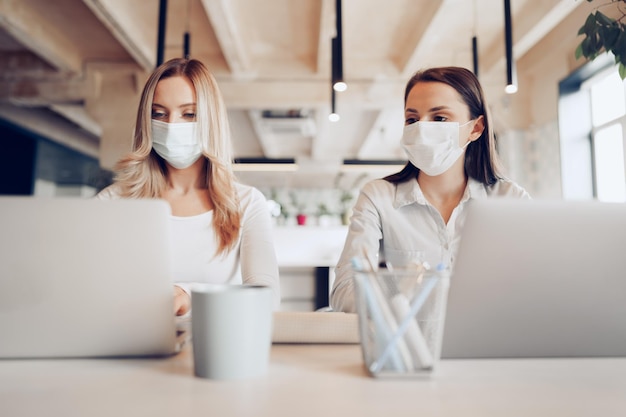 Photo two female colleagues working in office together wearing medical masks