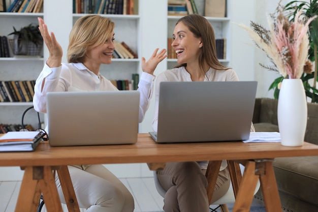 Two female collegues working with laptop and discussing new project.