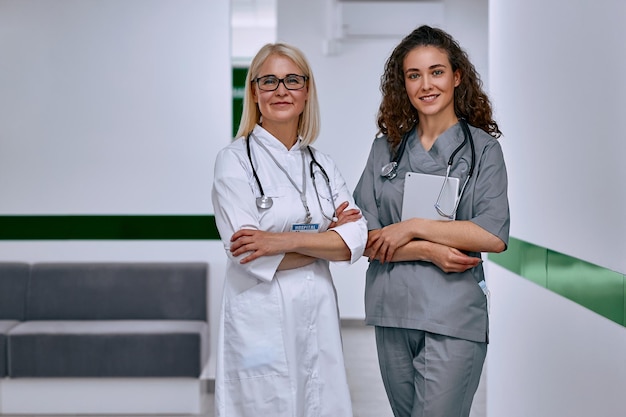 Two female doctors in the corridor of the clinic stand and look at the camera Health care