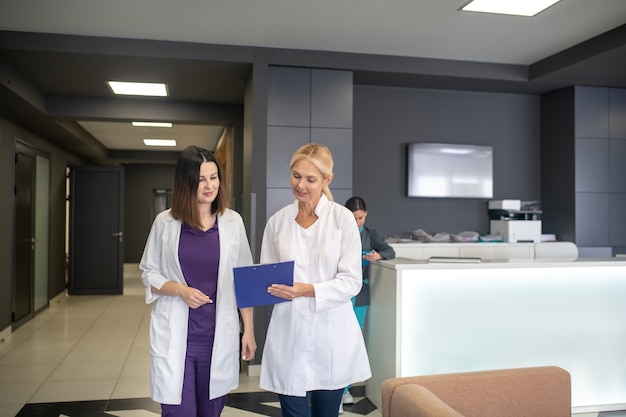 Two female doctors looking busy talking in the clinic corridor