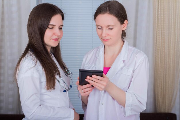 Two female doctors or nurses look at the tablet and discuss therapy