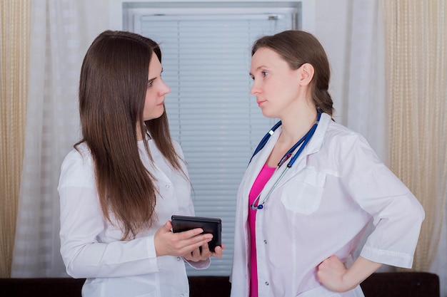 Two female doctors or nurses look at the tablet and discuss therapy