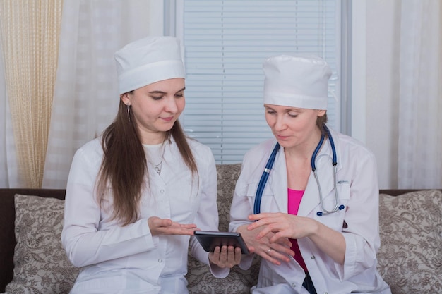 Two female doctors or nurses look at the tablet and discuss therapy