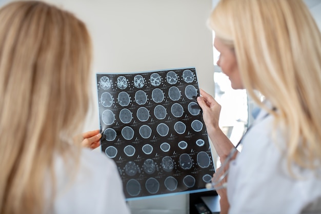 Two female doctors standing with their backs to camera looking at MRT scan holding it in their hands meditating