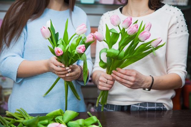 フラワーショップで休日のチューリップの花束を作る2人の女性の花屋デザイナー。花の装飾プロセス