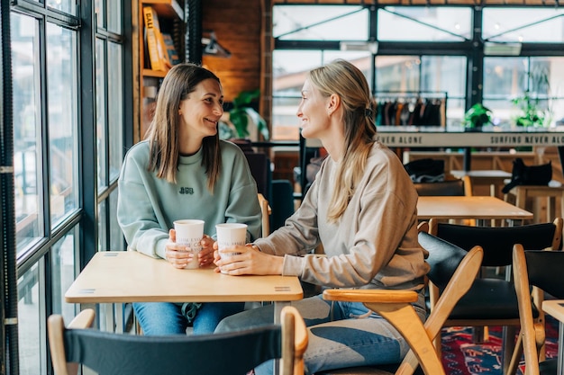 Photo two female friends are chatting and drinking coffee while sitting in a coffee shop