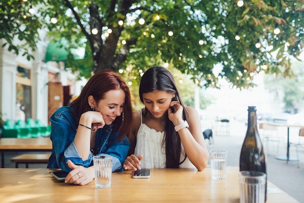 Two female friends browsing in mobile phones at street cafe