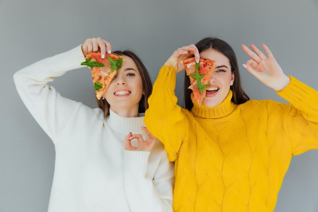 Two female friends holding pizza slices. Young people having fun eating dinner.