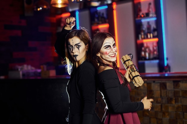 Two female friends is on the thematic halloween party in scary makeup and costumes with time bomb.