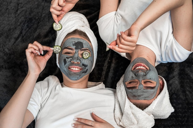 두 명의 여성 친구가 얼굴 마스크와 눈 주위 피부의 신선함을 위해 호박을  ⁇ 어서 바닥에 누워 있습니다. 피부 관리 또는 자연 관리 미용 치료