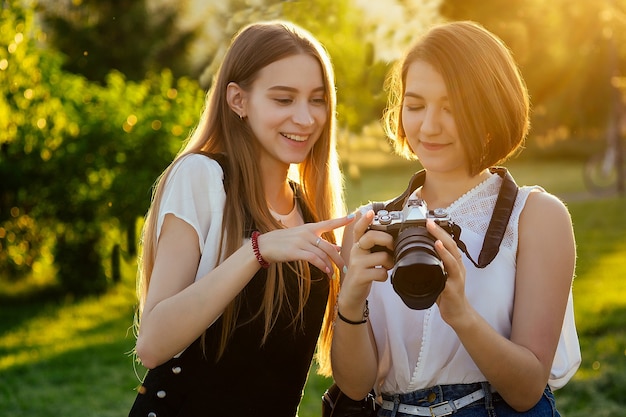 Two female friends in the park photographing on a professional camera . photo shoot photosession in the city.