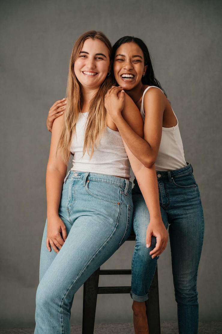 Photo two female friends posing in the studio sharing a stool
