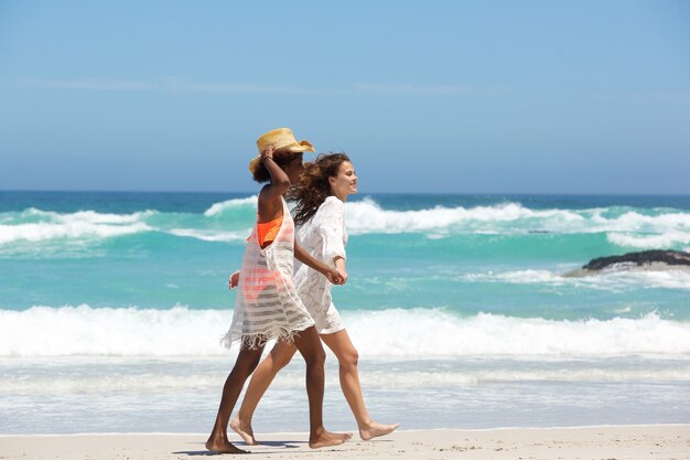 Two female friends walking on beach together 