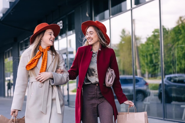 Two female friends walking by street with shopping bags in hands