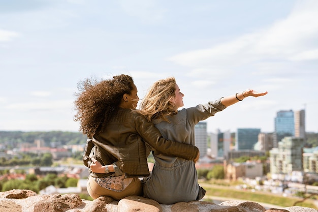 Two female friends waving their hands and enjoying the city skyline view concept