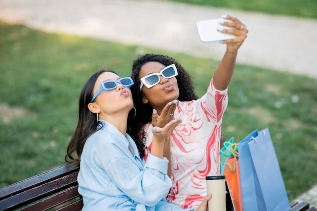 Foto due amiche con borse della spesa che si fanno selfie mentre si rilassano all'aperto